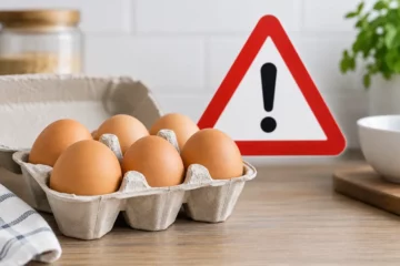 Ilustracja redakcyjna: tacka z jajami na blacie i symbol ostrzegawczy w tle, nieprzedstawiająca rzeczywistej partii objętej alertem.